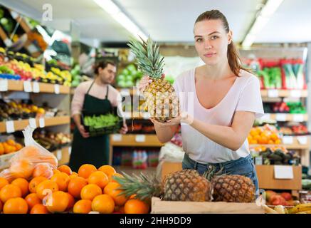 Young woman customer holding fresh pineapples in hands Stock Photo