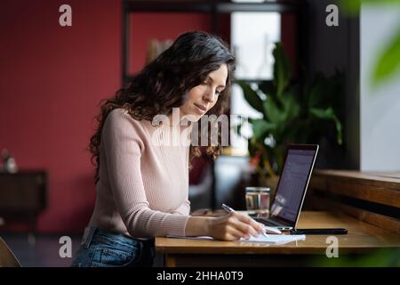 Focused young woman auditor doing paperwork at workplace in office, preparing financial statement Stock Photo
