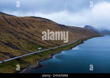 A virtually empty road in the Faroe Islands surrounded only by grassy mountains and the sea. Stock Photo