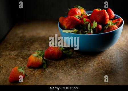 A blue bowl of fresh strawberries with dark and moody lighting Stock Photo