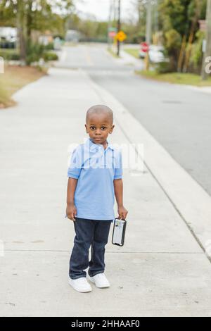 A little boy standing outside holding a cell phone and looking sad Stock Photo