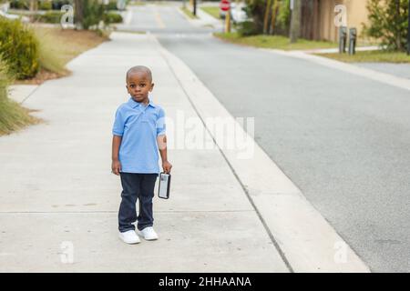 A little boy standing outside holding a cell phone and looking sad Stock Photo