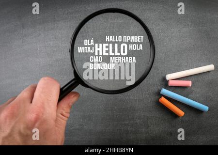 Hello. Text in different world languages. Magnifying glass on a dark blackboard background. Stock Photo
