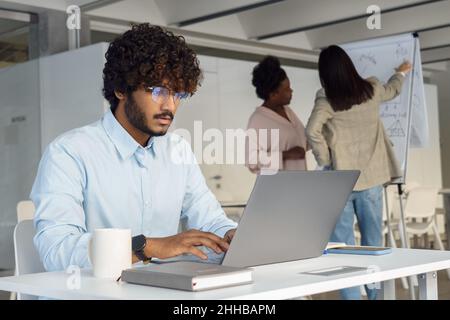 Serious indian man working on laptop at startup team open space office Stock Photo