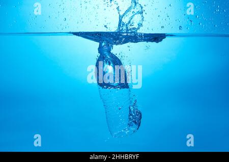Blue background with water bottle falling in and multiplle drops and splashed. Water bubbles texture Stock Photo