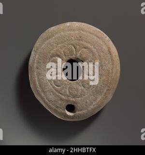 Terracotta oil lamp late 5th–6th century A.D. Roman Vessberg Type 20. Mold-made. Deep, lentoid shape, with impressed decoration. Large, oval central filling hole, surrounded by a rosette pattern comprising seven circular petals, interspersed with indistinct tongues; towards edge, two concentric grooves, the outer one broken by the front edge of the wick hole. On the uneven base, traces of circular grooves.Intact.. Terracotta oil lamp  241600 Stock Photo