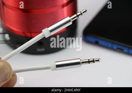 Aux cable or close-up of silver 3.5mm audio jack cable with the smartphone and external speaker on the background. Home Music concept Stock Photo