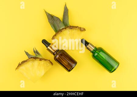 two bottles of green and brown glass with a pipette with pineapple extrate on a yellow background with fruit slices. top view