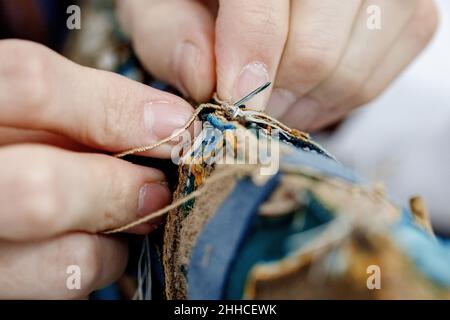 Closeup hands of craftsman tailor sewing with a needle and thread. Dressmaker is in process of working. Stock Photo