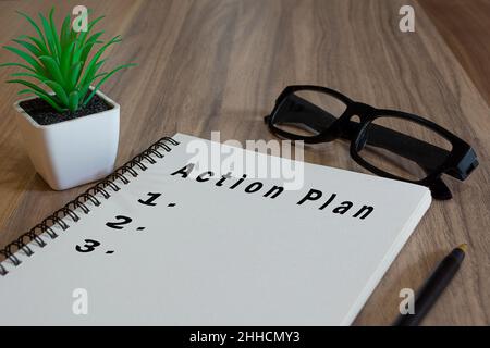 Action plan text on white notepad with potted plan, glasses and a pen on wooden desk Stock Photo