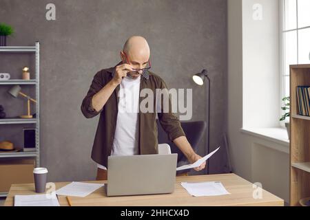 Man looks in surprise through his glasses at bills for payment, bank statement or debt on loan. Stock Photo