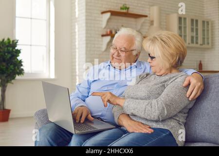 Happy senior couple shopping online and reading news using laptop while sitting on sofa at home. Stock Photo