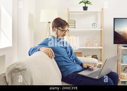 Young caucasian man sit on sofa browse laptop Stock Photo