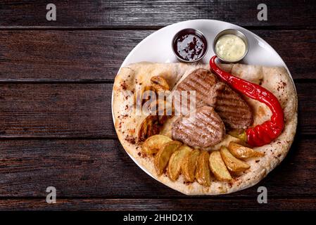 Delicious juicy chicken steak with baked potatoes, mushrooms and sauces on a white dish Stock Photo