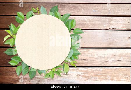 Green leaves and round paper card on wood texture. Horizontal banner with eco paper texture. Wooden planks, recycled carton material label and green l Stock Photo