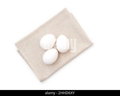 Three chicken eggs on kitchen towel, isolated on white, top view Stock Photo