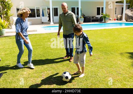 Caucasian grandparents and grandson playing football together in garden Stock Photo