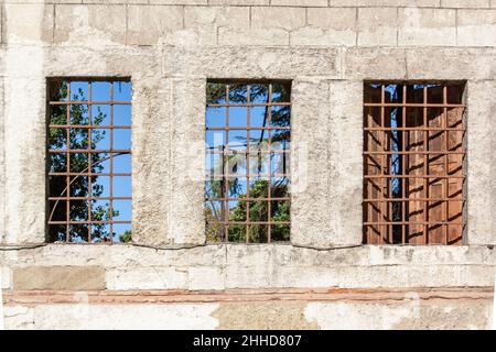 Three windows with bars in block wall. One window has shutters. Stock Photo