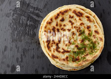 Flatbread with cheese and herbs on a dark stone table Stock Photo