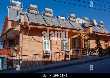 A lot of solar water heating systems on roof of house. A lot of large water tanks and solar panels on roof. Stock Photo