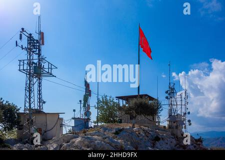 Many antennas of cell towers with transmitters standing on hill along withTurkish flag in background of sky with clouds. Stock Photo