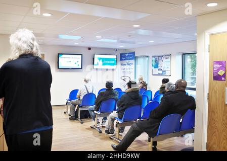 Person standing at reception while a busy waiting room in a health centre is busy and full with people sitting Stock Photo