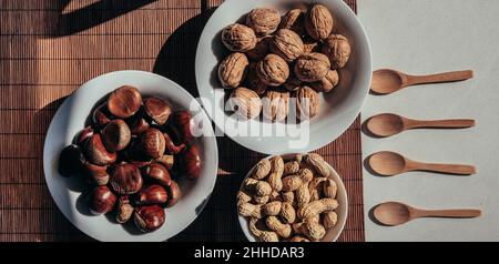 Top view of bowls with various nuts placed on bamboo mat near wooden spoons on table in kitchen Stock Photo
