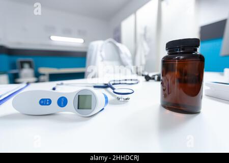 Selective focus on medical tools standing on table in empty doctos office ready for health care support. Hospital workplace with nobody in it having professional infrared thermometer. Medicine service Stock Photo