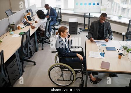 High angle portrait of successful businesswoman using wheelchair while managing at business meeting in office and talking to team, copy space Stock Photo