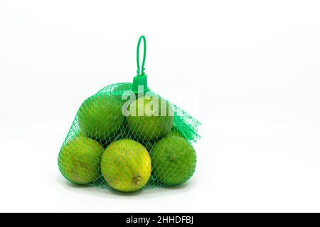 Seedless green lemons in a mesh bag, isolated organic green lemons on white background. Stock Photo
