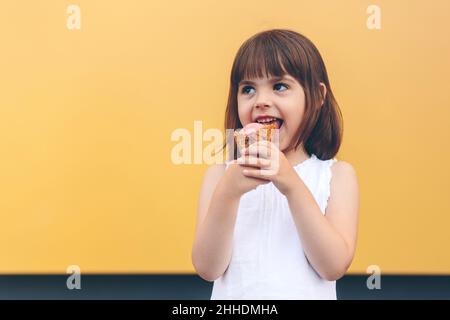 Little happy baby girl eating chocolate ice cream, on yellow background Stock Photo