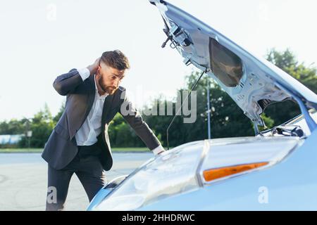 an annoyed and angry man, near a broken car, tries to call an insurance agent and a repair crew. for car repair Stock Photo