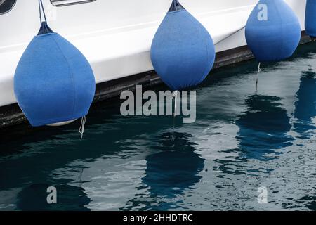 Yacht fender. Luxury boat anchored at the marina detail, blue rubber bumper, reflection on sea water Stock Photo