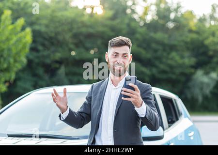 Successful and happy man brags about buying a new car, having fun talking to friends uses a video call in the phone app Stock Photo