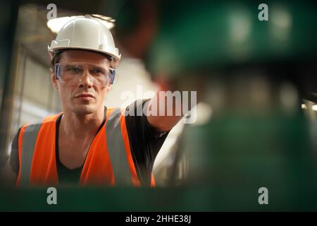 Factory Engineer Operating Hydraulic Tube machine. Men industrial engineer wearing a white helmet while standing in a heavy industrial factory behind. Stock Photo