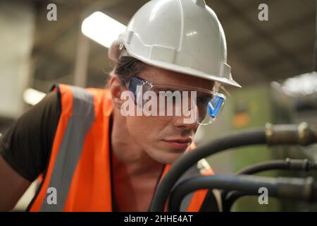 Factory Engineer Operating Hydraulic Tube machine. Men industrial engineer wearing a white helmet while standing in a heavy industrial factory behind. Stock Photo