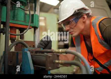 Factory Engineer Operating Hydraulic Tube machine. Men industrial engineer wearing a white helmet while standing in a heavy industrial factory behind. Stock Photo