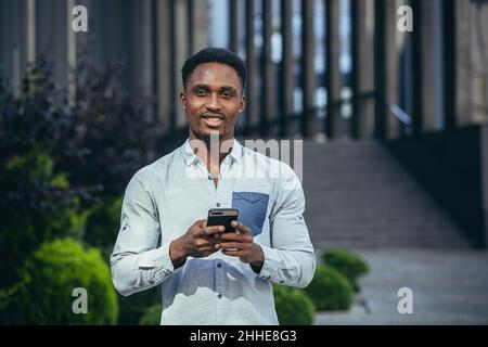 Charming african american man happy looking at camera, holding mobile phone in hands smiling and happy Stock Photo