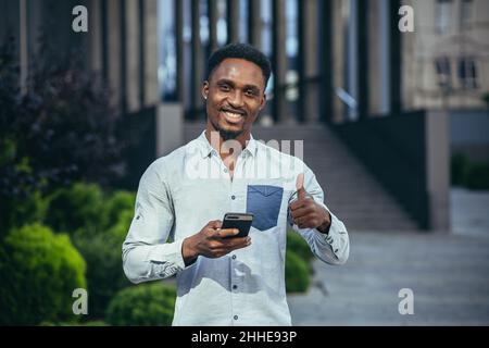 Charming african american man happy looking at camera, holding mobile phone in hands smiling and happy Stock Photo
