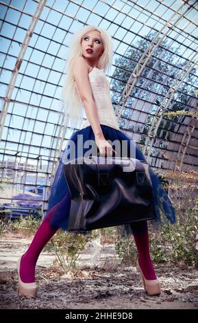 Portrait of the lovely freak girl with old suitcase. Beautiful woman wearing colorful corset, tights and tutu skirt in forsaken place Stock Photo