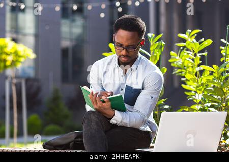 Student studies online remotely, African American man smiles and rejoices, takes online courses uses laptop Stock Photo