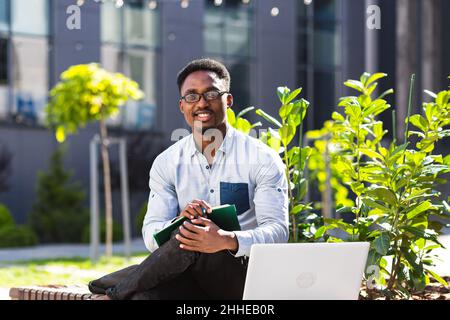 Student studies online remotely, African American man smiles and rejoices, takes online courses uses laptop Stock Photo