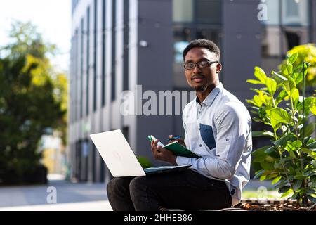 Student studies online remotely, African American man smiles and rejoices, takes online courses uses laptop Stock Photo