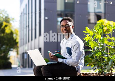 Student studies online remotely, African American man smiles and rejoices, takes online courses uses laptop Stock Photo