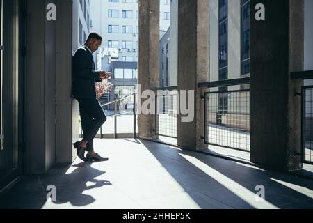 Male businessman near office reads news from tablet computer, african american freelancer in business suit near office outside Stock Photo