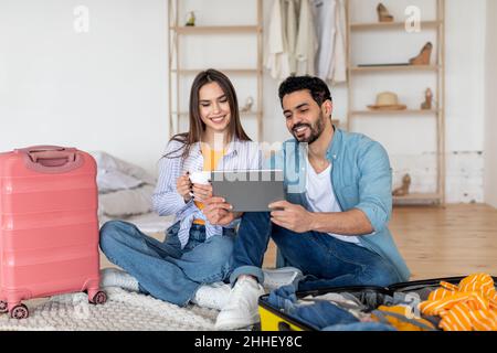 Happy tourists couple using digital tablet and booking travel tickets, choosing destination for next vacation online Stock Photo