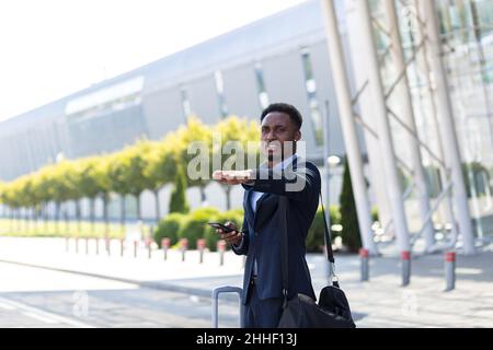 Male businessman near airport with suitcase, african american trying to catch taxi car Stock Photo