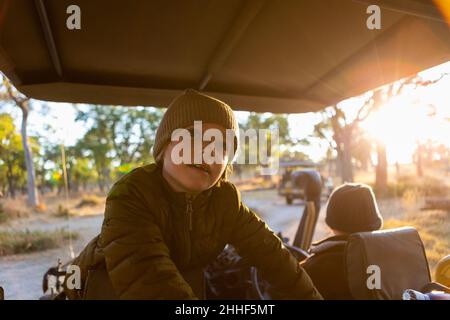 A boy sitting in a jeep on a safari drive at sunrise Stock Photo