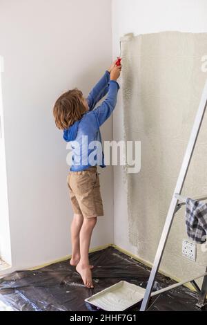 Eight year old boy using paint roller to paint a house wall Stock Photo