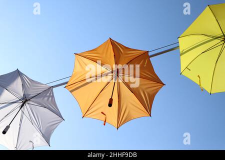 Orange, white and yellow umbrellas hanging against clear blue summer sky, come rain or shine concept Stock Photo